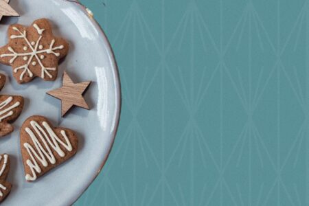 Plate of iced gingerbread cookies with pine branches on a teal background