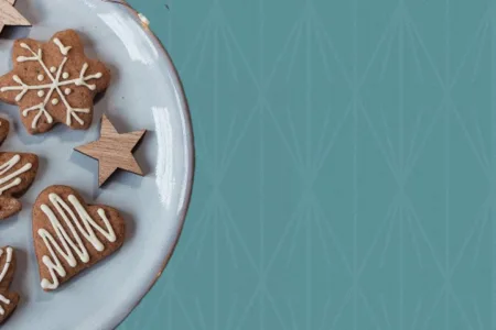 Plate of iced gingerbread cookies with pine branches on a teal background